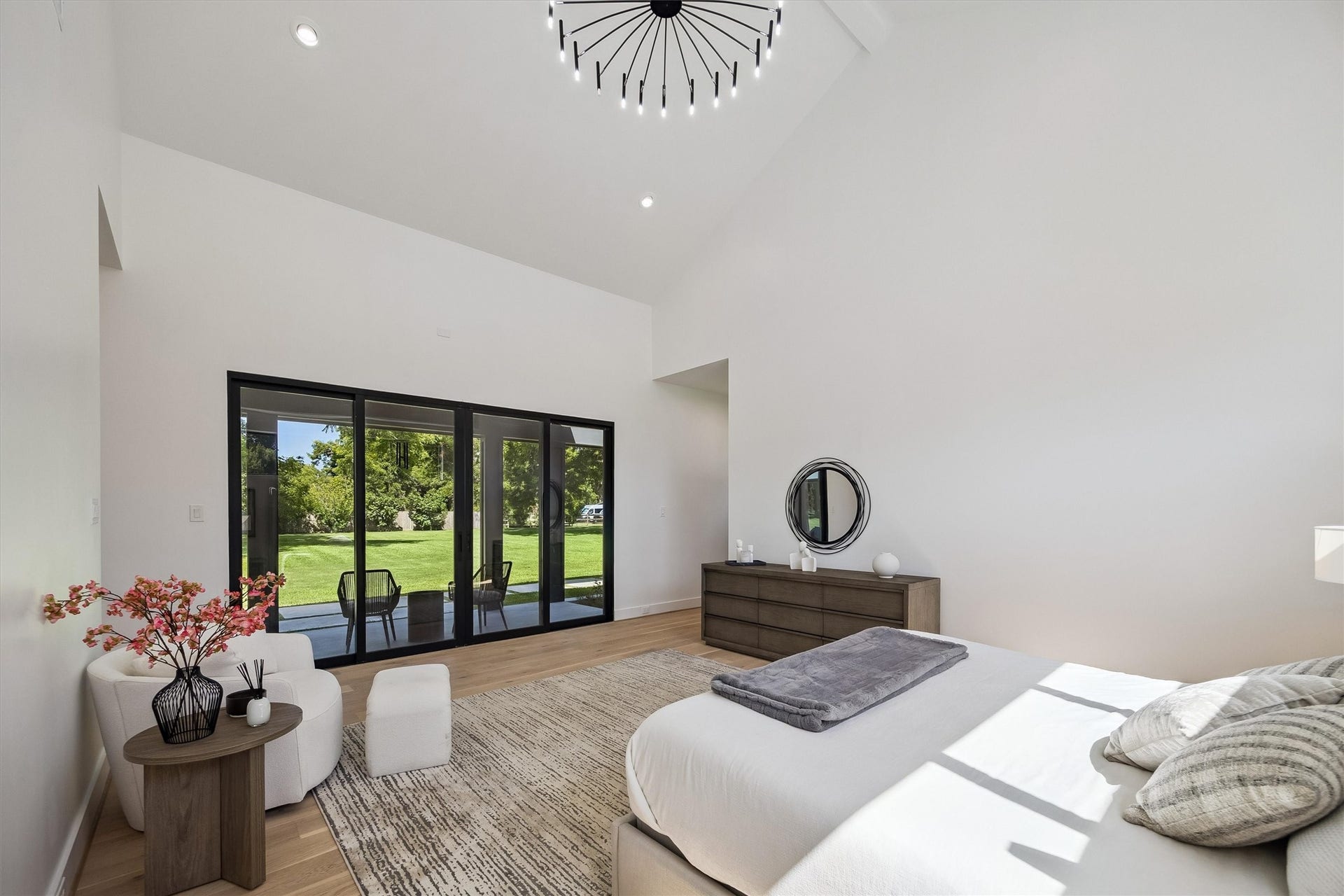 5210 Manor Drive, Sugar Land, TX 77479 Spacious bedroom with high ceilings and abundant natural light, featuring a modern chandelier, sleek furniture, and large sliding glass doors opening to a lush backyard view.