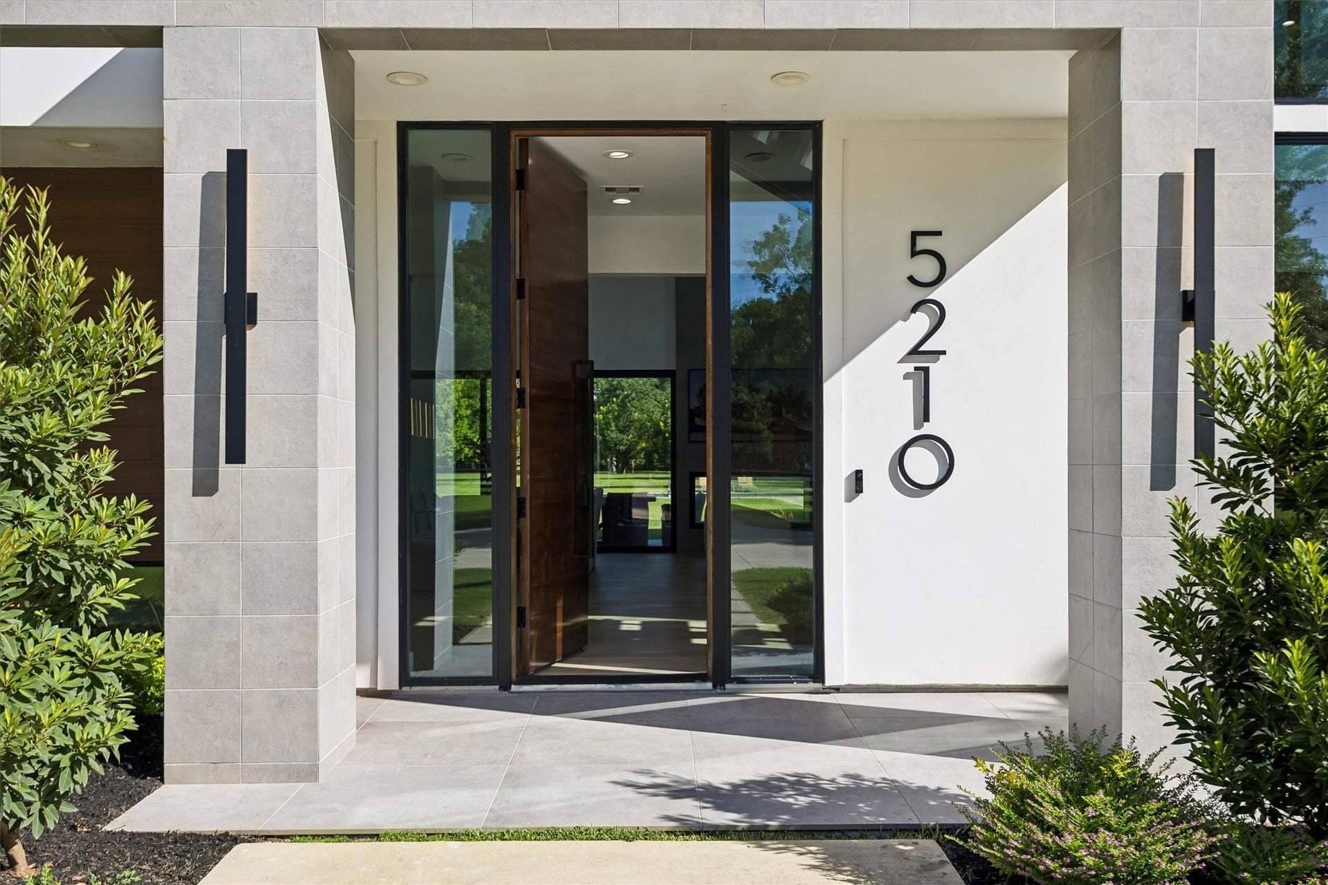 5210 Manor Drive, Sugar Land, TX 77479 Stunning modern entryway with sleek architectural lines, large glass door, and elegant landscaping, offering a warm welcome with an open view to the lush greenery beyond.