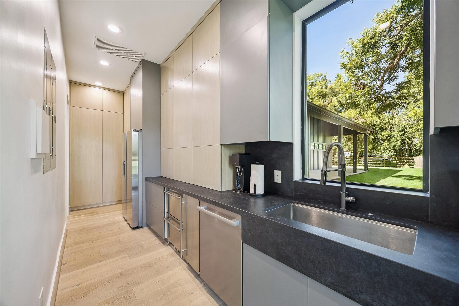 5210 Manor Drive, Sugar Land, TX 77479 Sleek modern kitchen with stainless steel appliances, ample cabinetry, and a large window offering serene views of the lush backyard.
