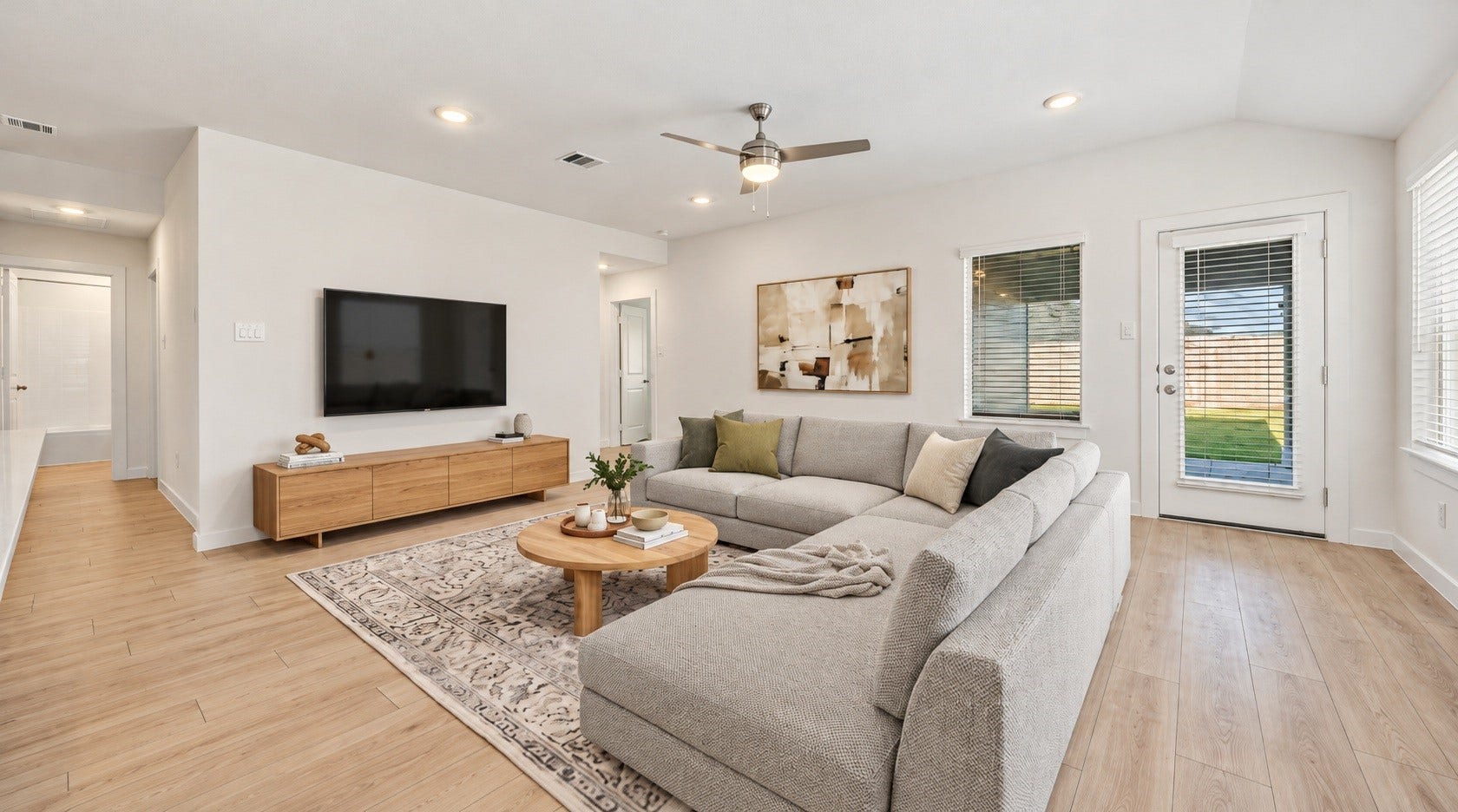 The open living area features wood-look flooring, a ceiling fan, and a door leading out to the backyard, creating a bright and inviting space. Virtually staged.