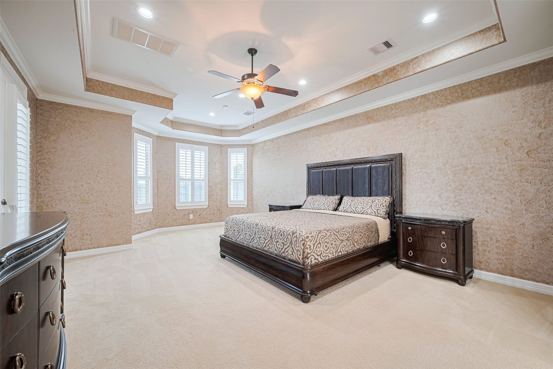 4722 Burclare Court, Sugar Land, TX 77479 Expansive primary suite enhanced by an intricate tray ceiling, textured finishes, and a sunlit bay of plantation-shuttered windows.