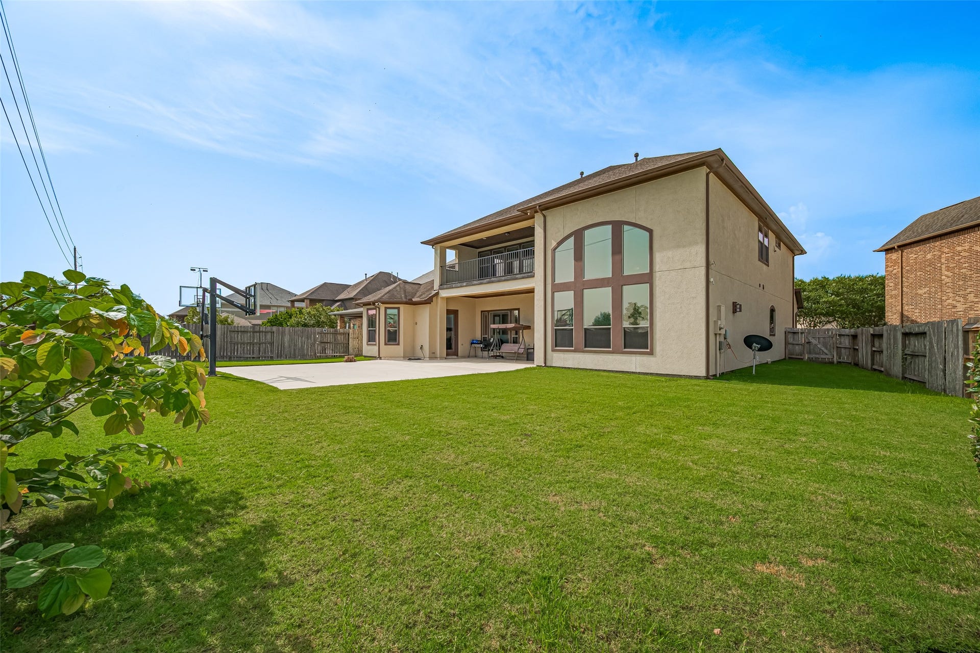4722 Burclare Court, Sugar Land, TX 77479 Expansive fenced backyard with a lush lawn, basketball court, covered patio, upper balcony, and striking rear elevation with dramatic oversized windows.