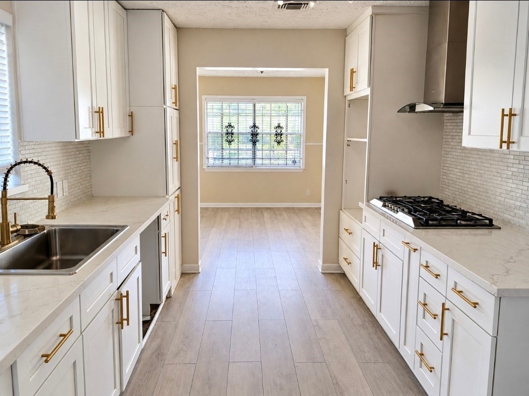 7929 Talton Street, Houston, TX 77028 Bright and modern kitchen featuring sleek white cabinetry with gold hardware, a stylish backsplash, and stainless steel appliances, leading to a cozy dining area with natural light.