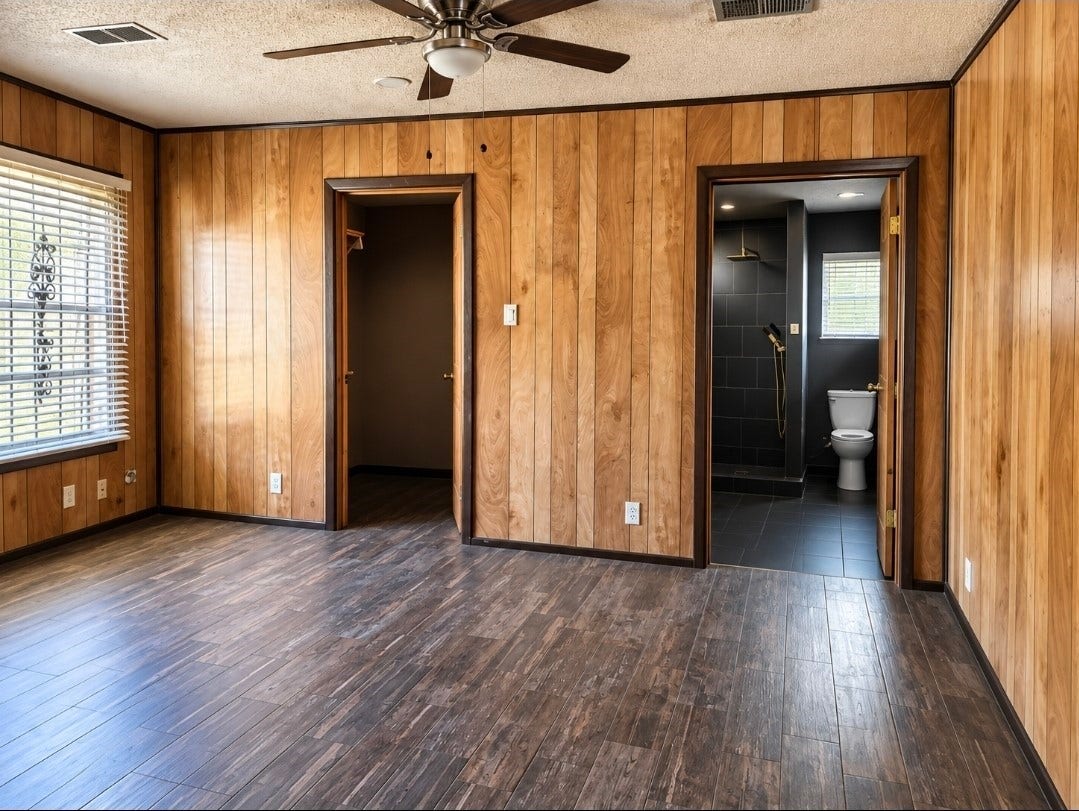 7929 Talton Street, Houston, TX 77028 Spacious room with rich wood paneling, hardwood floors, and a ceiling fan, featuring an ensuite bathroom with sleek black tile and modern fixtures.