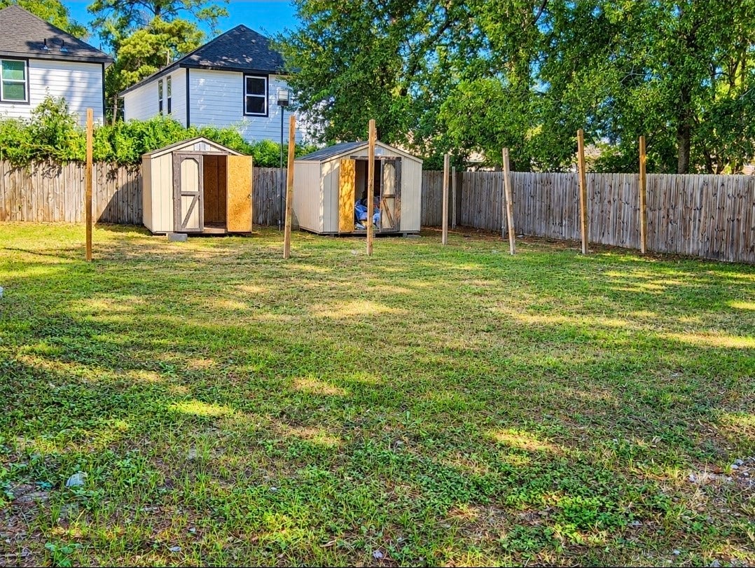7929 Talton Street, Houston, TX 77028 Spacious backyard with lush grass, fenced for privacy, featuring two storage sheds and surrounded by mature trees.
