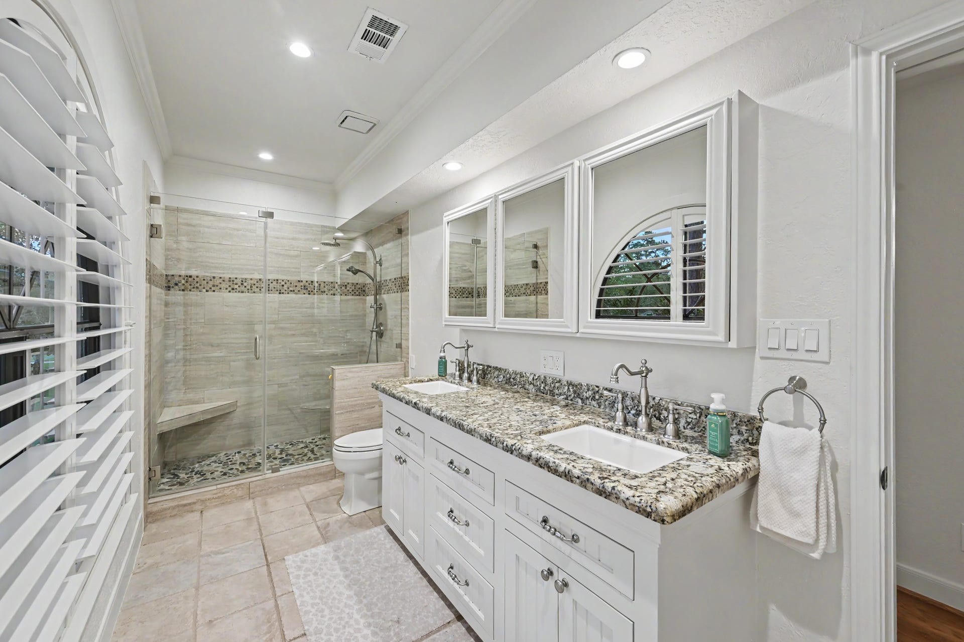 Well-appointed secondary bath featuring a dual-sink granite vanity, plenty of cabinetry, and a spacious glass-enclosed walk-in shower.