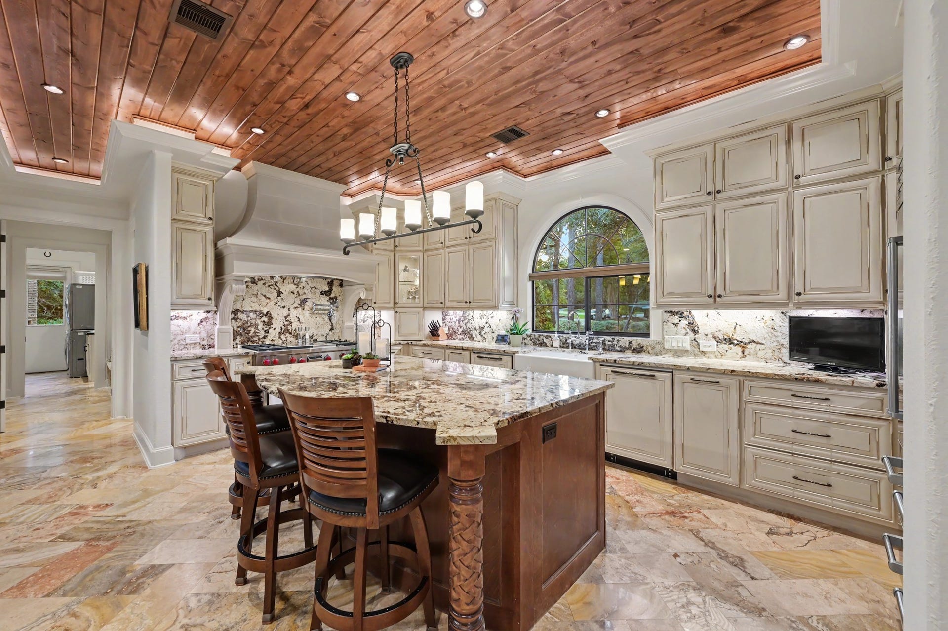 Impressive chefs kitchen featuring custom cabinetry, expansive granite island, professional-grade range, and a striking wood-plank ceiling that adds warmth and character.