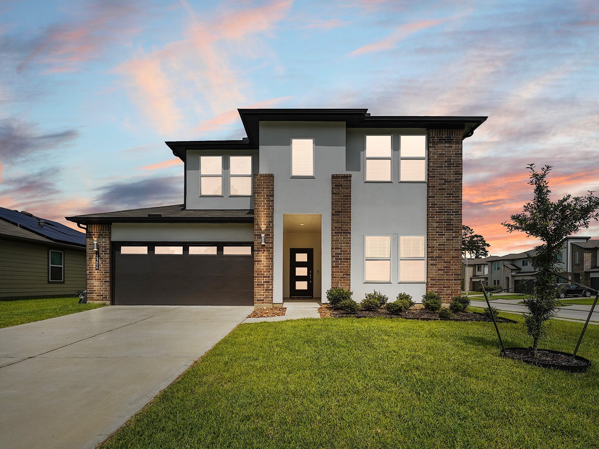 Modern two-story home with a sleek design, featuring a mix of brick and stucco exterior, a spacious driveway, and a well-maintained lawn.