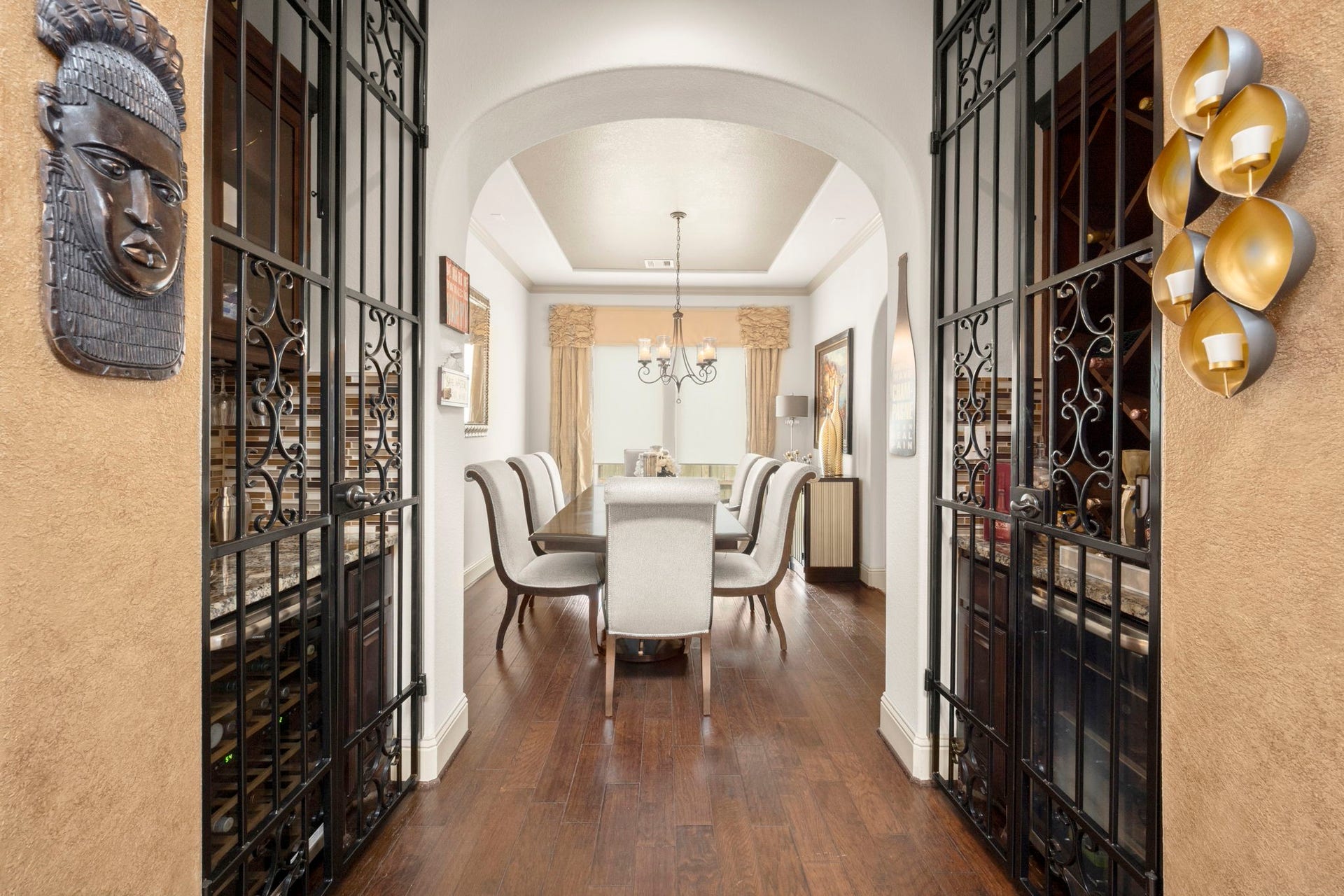 5103 Jackson Ponds Court, Sugar Land, TX 77479 A designated dining area with rich wooden flooring and a sophisticated chandelier. The entryway of the room features a bar and wine cabinet framed by decorative iron gates.