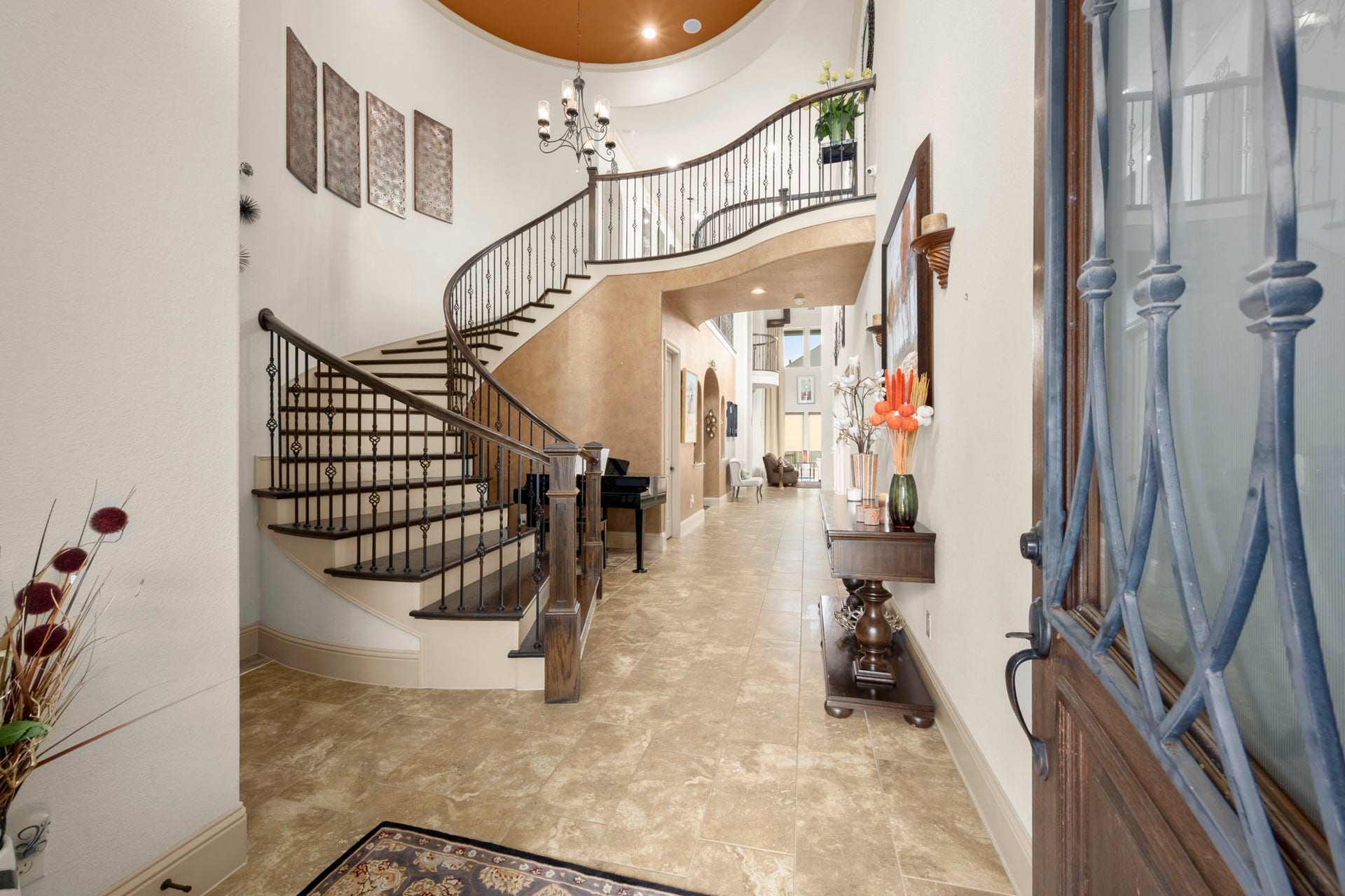 5103 Jackson Ponds Court, Sugar Land, TX 77479 The home features an elegant foyer with a grand, curved staircase and wrought iron railing. This space also features high ceilings and a chandelier that leads into a well-lit hallway with tile flooring.