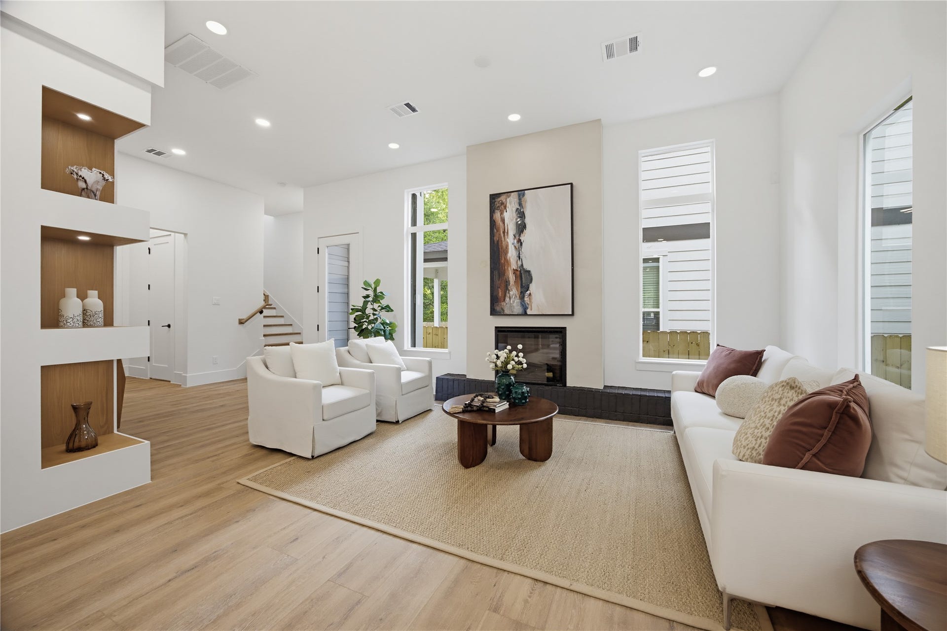 1004 E 35th Street, Houston, TX 77022 Modern living room with high ceilings, featuring a cozy fireplace and abundant natural light from tall windows. The open layout includes elegant built-in shelving and warm wood flooring, creating a welcoming ambiance.