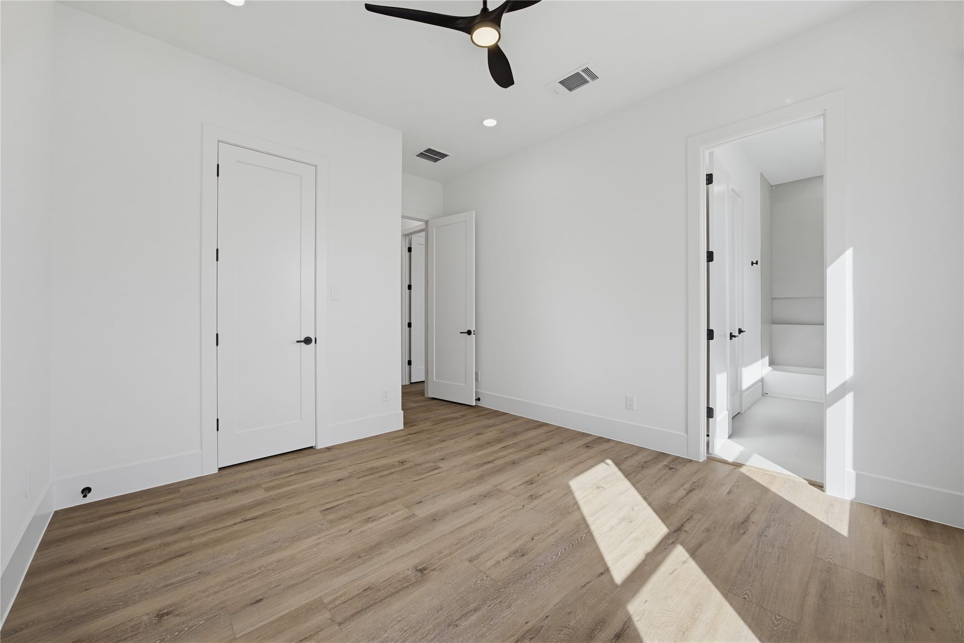 1004 E 35th Street, Houston, TX 77022 Bright and airy 2nd bedroom featuring sleek hardwood floors, modern ceiling fan, and ample natural light, with convenient access to an ensuite bathroom.