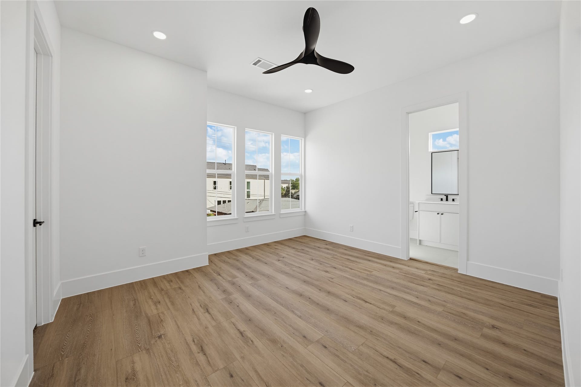 1004 E 35th Street, Houston, TX 77022 Bright and airy 3rd bedroom featuring large windows, sleek ceiling fan, and elegant wood flooring, leading to an en-suite bathroom.