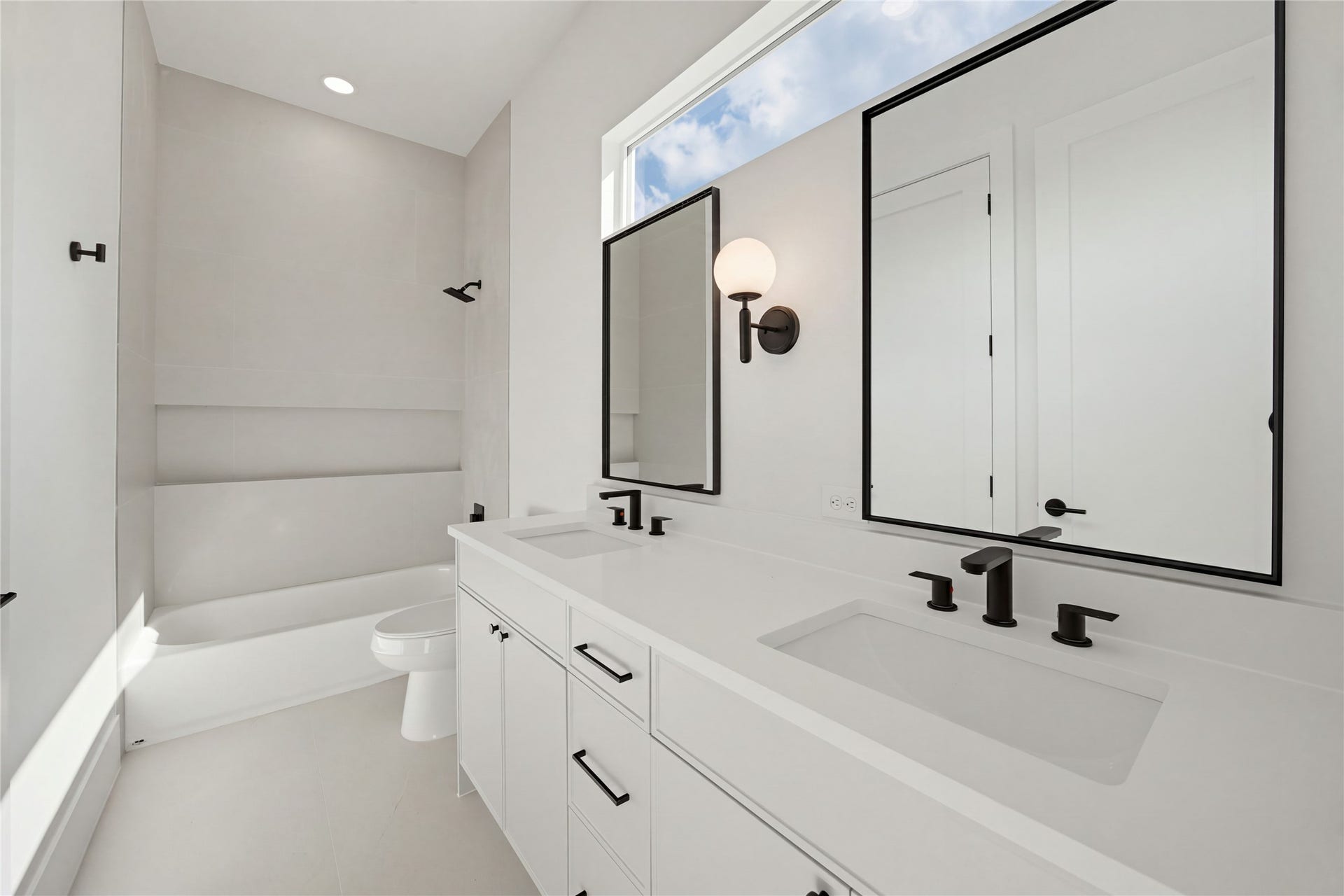 1004 E 35th Street, Houston, TX 77022 Sleek and modern bathroom featuring a double vanity with black fixtures, a spacious tub, and abundant natural light from a large window.