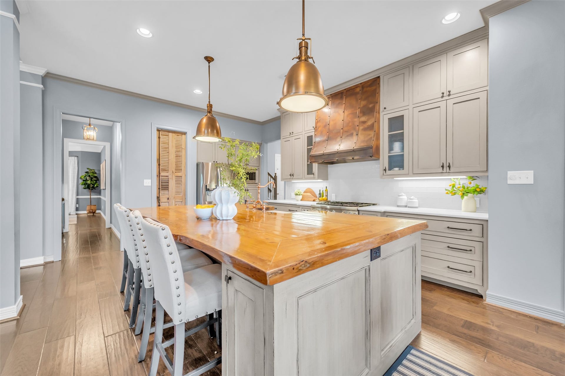 8703 Stones Throw Lane, Missouri City, TX 77459 This kitchen is a chef's dream featuring recessed lighting, copper pendant lighting, glass front and custom cabinets, copper vent hood and island with an exotic wood living-edge countertop.
