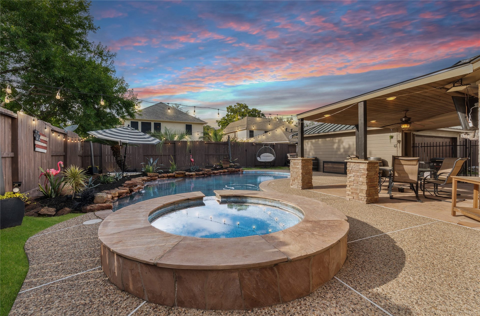2437 La Rochelle Court, Seabrook, TX 77586 Resort-inspired backyard with a sparkling pool, raised spa, covered patio, and evening string lights.