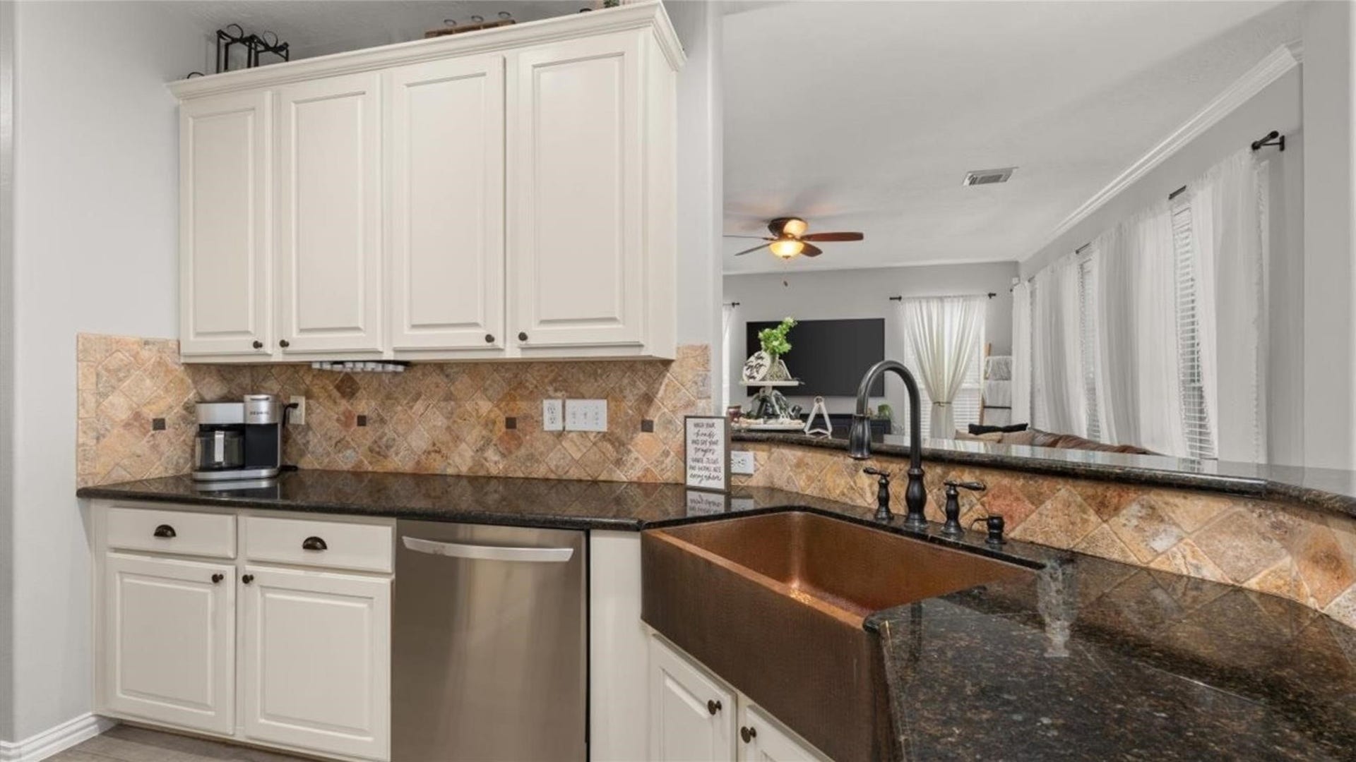 2437 La Rochelle Court, Seabrook, TX 77586 White cabinetry and granite counters complement the copper farmhouse sink and stainless steel dishwasher.
