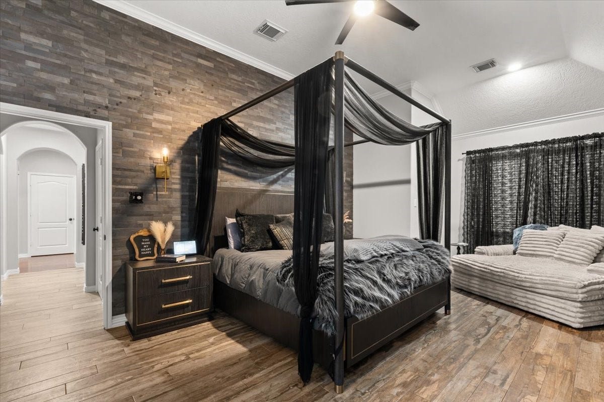 2437 La Rochelle Court, Seabrook, TX 77586 The spacious primary bedroom features a dramatic stone accent wall, canopy bed, and sitting area.