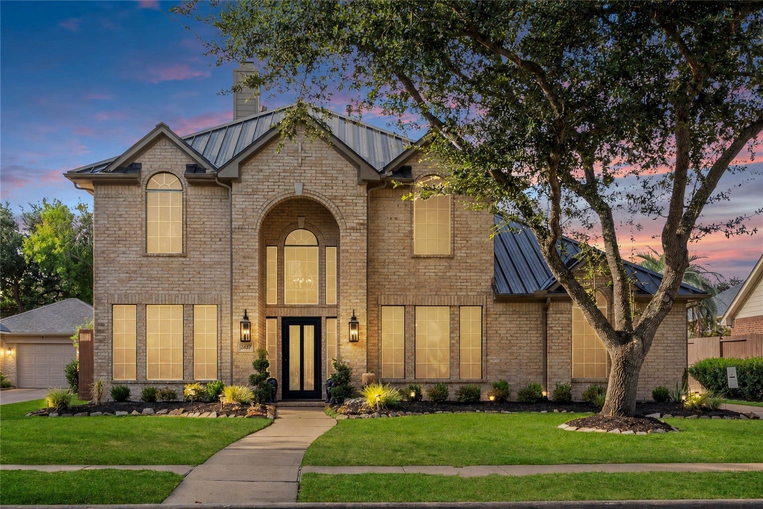 2437 La Rochelle Court, Seabrook, TX 77586 Welcome to 2437 La Rochelle Ct. Striking two-story brick exterior with a metal roof, mature landscaping, and welcoming illuminated entry.
