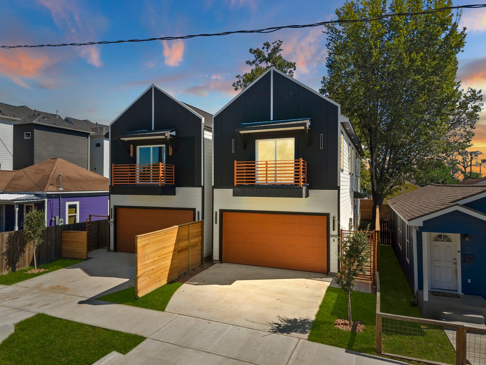 This striking two-story home features sharp gabled architecture and sleek modern paneling. Private upper balconies extend the living space outdoors, while an expansive concrete driveway and neatly landscaped yard provide generous off-street parking and excellent functional footprint.