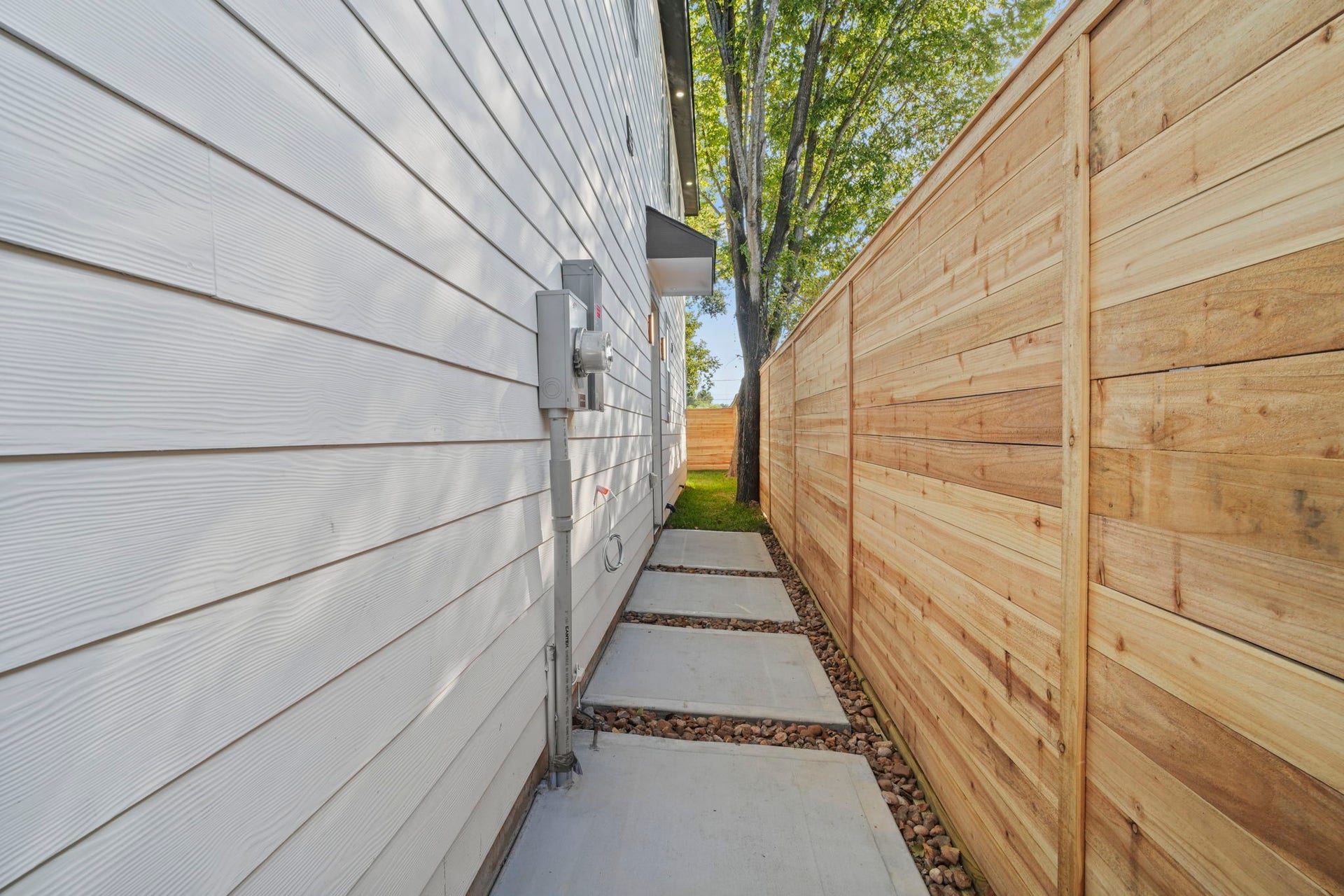 This private side pathway features modern horizontal wood fencing paired with clean concrete paver walkways framed by decorative gravel.