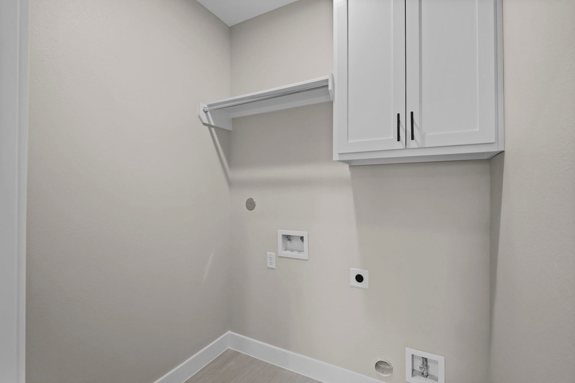 This dedicated laundry room features upper wall cabinetry and an attached hanging rod for easy organization and air-drying.