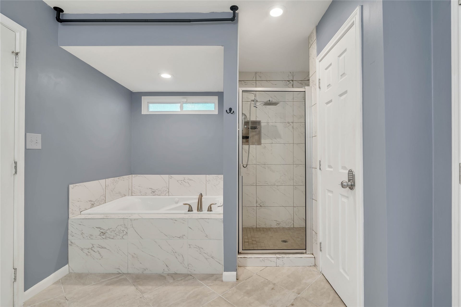 10818 Elmdale Drive, Houston, TX 77070 Relax in the spacious primary bath, featuring a deep soaking tub with marble-look tile surround, a separate tiled walk-in shower with rainfall showerhead, and a clean, contemporary design.