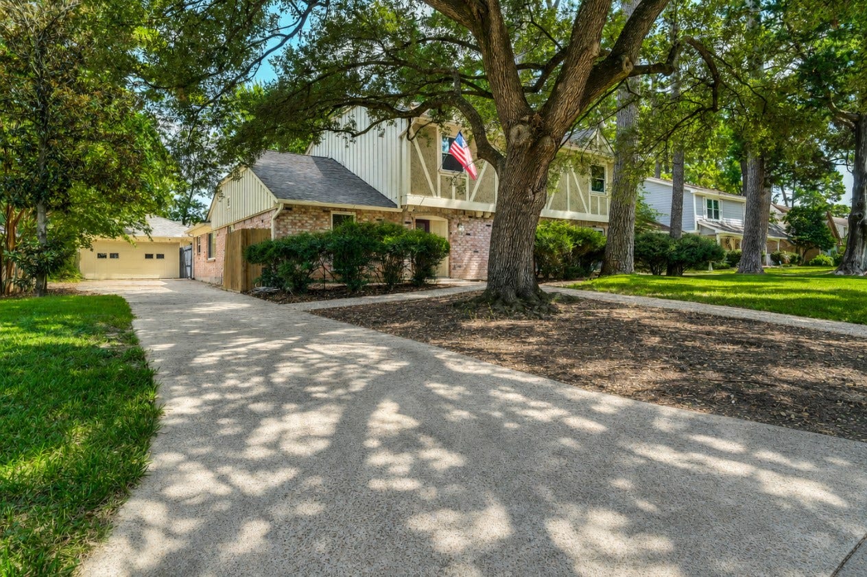 10818 Elmdale Drive, Houston, TX 77070 Side exterior view highlighting the extended driveway leading to the detached garage, surrounded by mature trees and established landscaping.