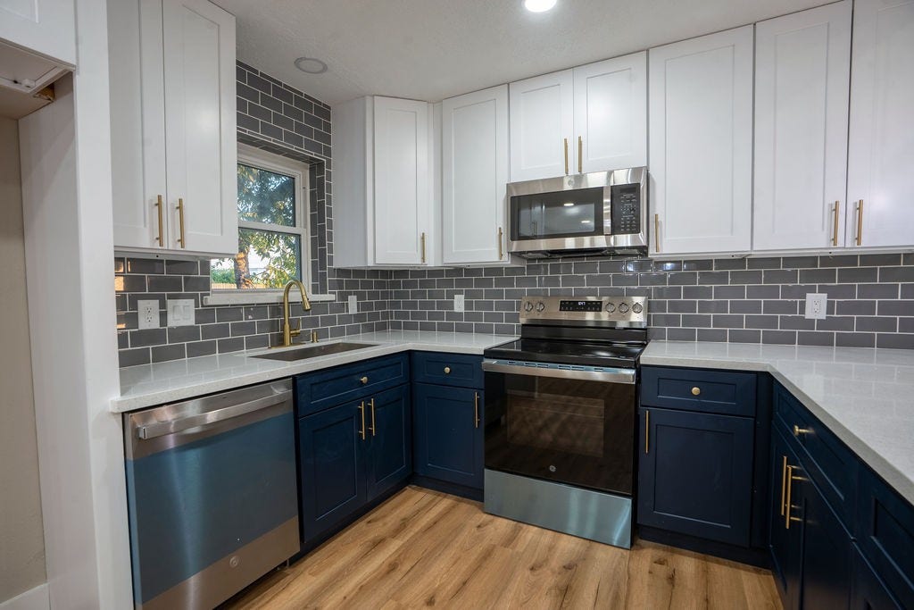 9856 Oriole, Conroe, TX 77385 Modern kitchen featuring sleek navy and white cabinetry, stainless steel appliances, and a stylish gray subway tile backsplash.
