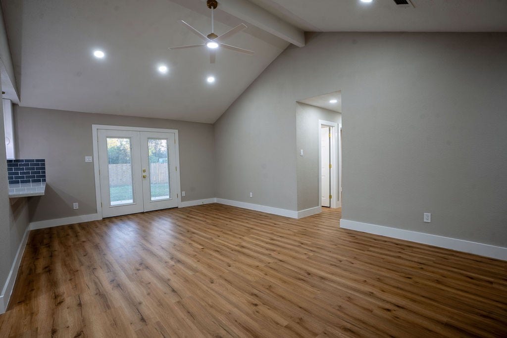 9856 Oriole, Conroe, TX 77385 Spacious living area with vaulted ceiling, stylish vinyl flooring, and elegant French doors leading to the backyard, perfect for natural light and outdoor access.