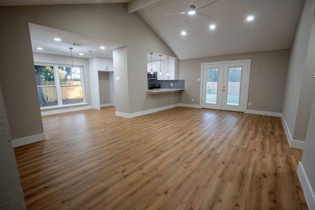 9856 Oriole, Conroe, TX 77385 Spacious open-concept living area with elegant wood style flooring, vaulted ceilings, and abundant natural light from large windows and French doors.