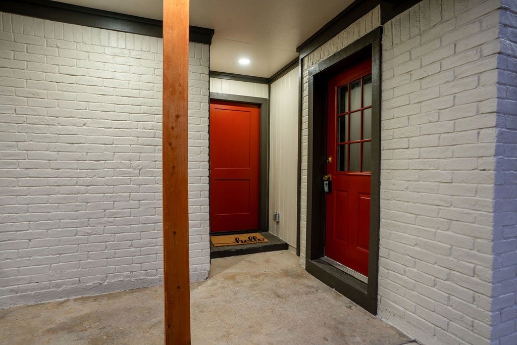 9856 Oriole, Conroe, TX 77385 Charming entrance with red doors and white brick walls, accented by a warm wood column and a welcoming doormat.