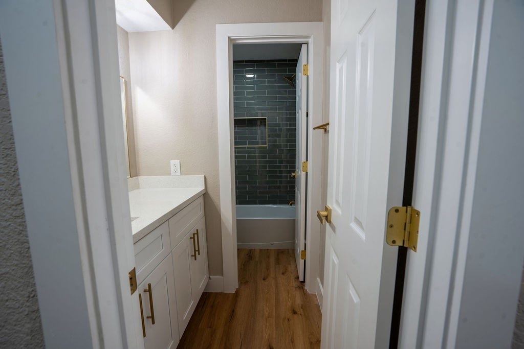 9856 Oriole, Conroe, TX 77385 Charming bathroom featuring a modern vanity with gold accents, sleek gray tile in the shower, and elegant wood style flooring for a warm touch.