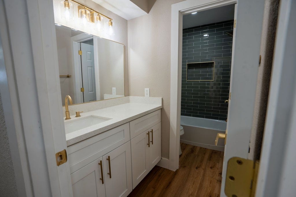 9856 Oriole, Conroe, TX 77385 Elegant bathroom featuring a sleek vanity with gold fixtures, a large mirror, and a modern subway-tiled shower area.