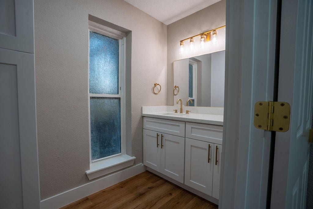 9856 Oriole, Conroe, TX 77385 Elegant bathroom featuring a stylish vanity with dual sinks, sleek brass fixtures, and a large mirror, complemented by a frosted window for privacy and natural light.