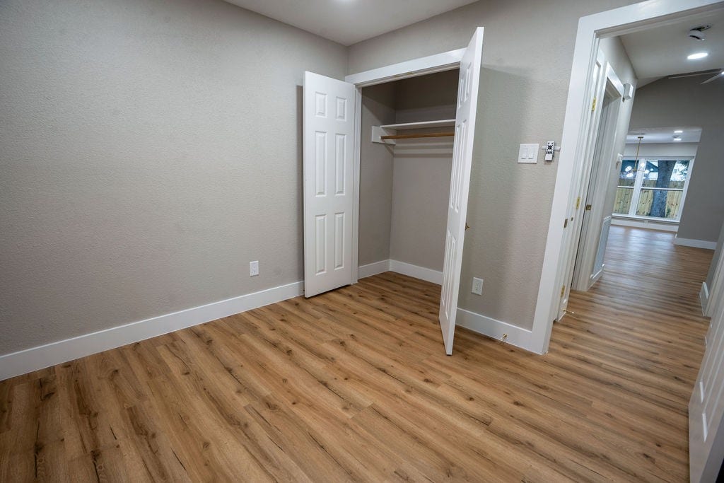 9856 Oriole, Conroe, TX 77385 Spacious room with sleek wood style flooring, a built-in closet, and a view into a bright hallway leading to a living area with large windows.