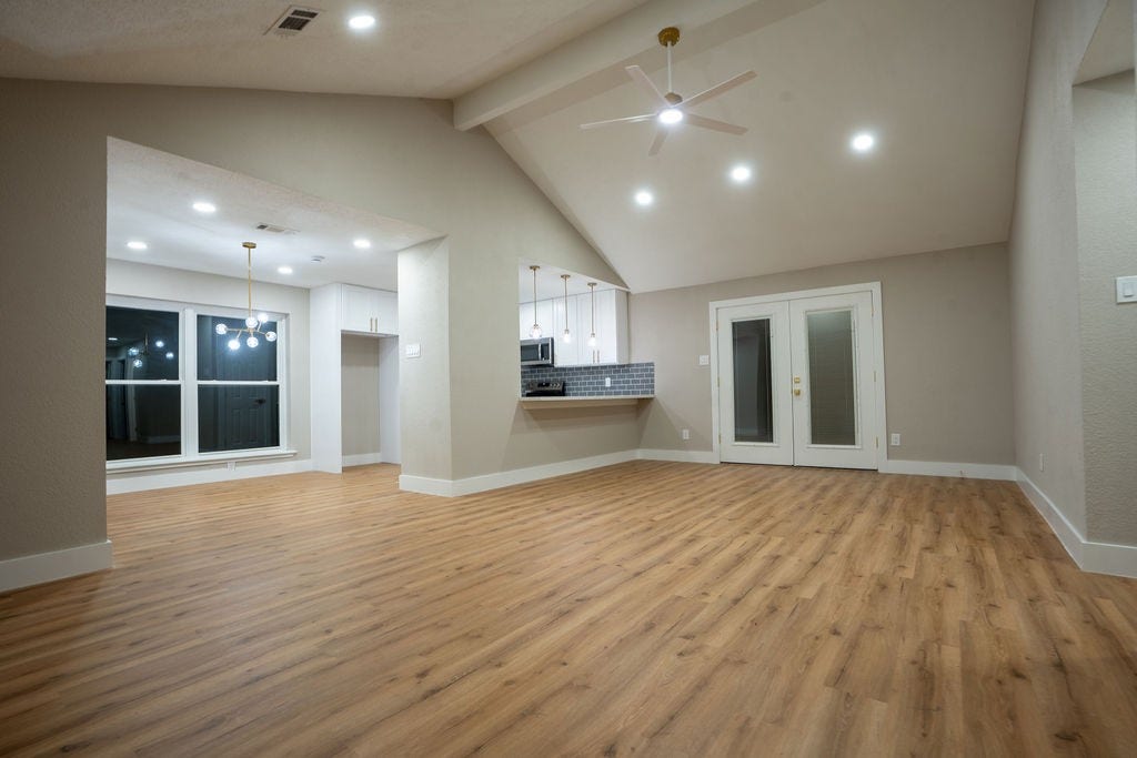 9856 Oriole, Conroe, TX 77385 Spacious open-concept living area with high vaulted ceilings, elegant vinyl flooring, and abundant natural light from large windows and double glass doors.