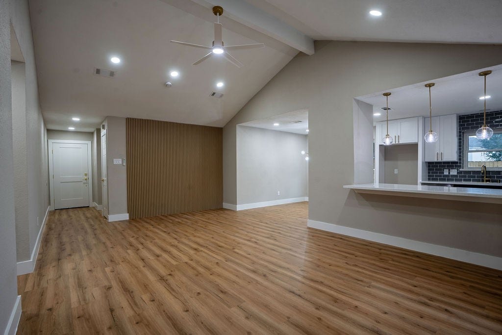 9856 Oriole, Conroe, TX 77385 Spacious living area with vaulted ceilings and recessed lighting, featuring a modern open layout with wood style flooring and a sleek kitchen with pendant lights and a breakfast bar.