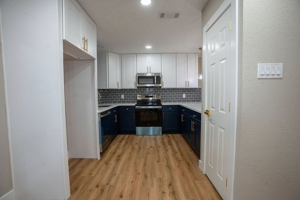 9856 Oriole, Conroe, TX 77385 Sleek kitchen featuring modern stainless steel appliances, elegant navy and white cabinetry, and a stylish gray subway tile backsplash, all complemented by warm wood style flooring.