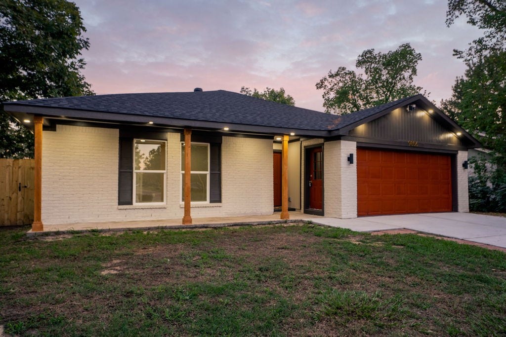 9856 Oriole, Conroe, TX 77385 Charming single-story home with modern exterior, featuring a sleek black roof and warm wood accents, complemented by a spacious two-car garage.