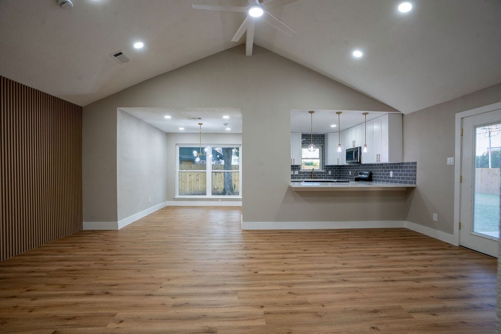 9856 Oriole, Conroe, TX 77385 Spacious open-concept living area with vaulted ceilings, elegant wood style flooring, and a modern kitchen featuring a stylish tile backsplash and pendant lighting.