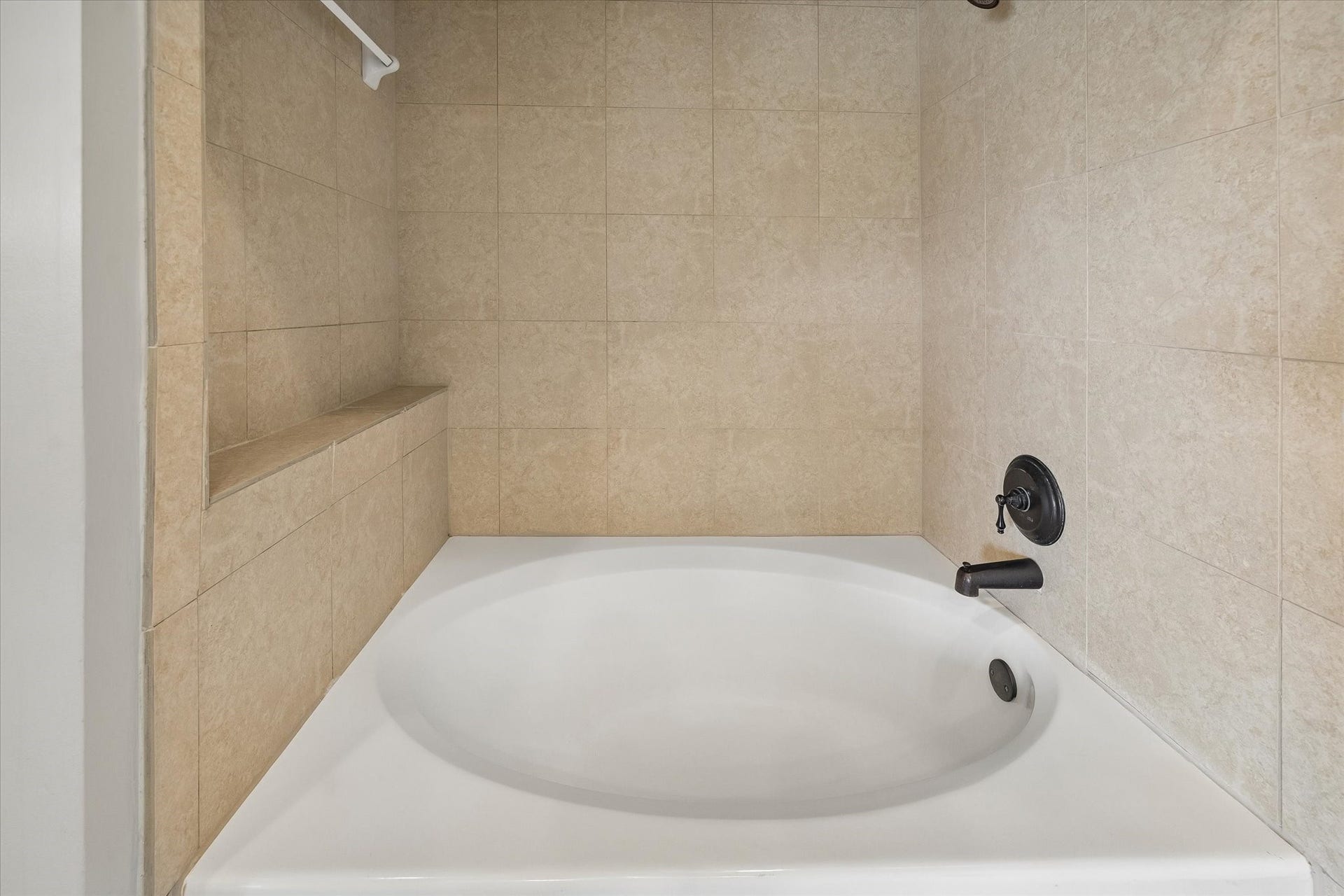 2203 Dorrington Street Street, #205, Houston, TX 77030 This bathroom features a modern tub with beige tile surround and a built-in shelf, offering a sleek and functional design.