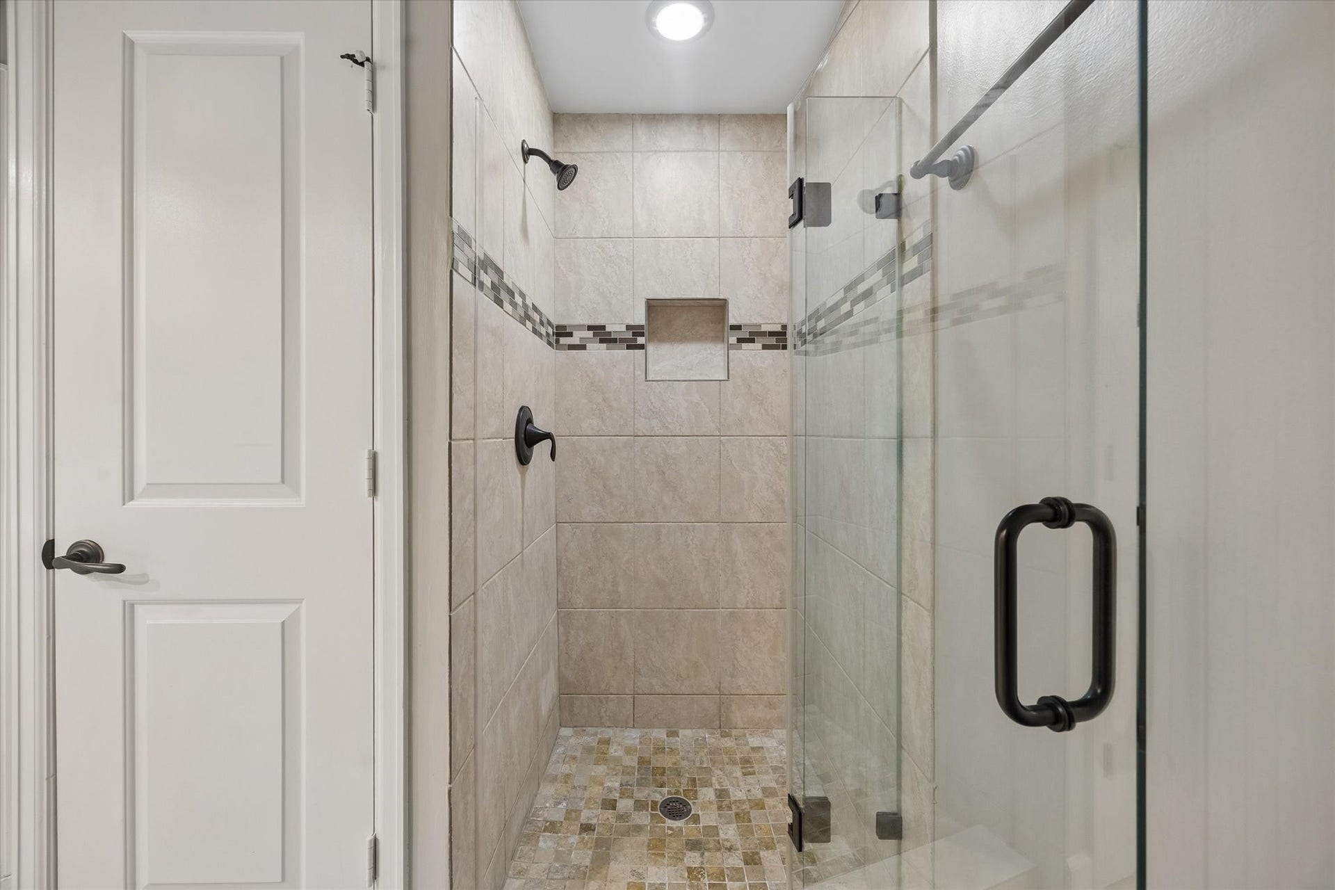 2203 Dorrington Street Street, #205, Houston, TX 77030 This photo shows a modern, tiled walk-in shower with a glass door, featuring a built-in niche and decorative tile accents.