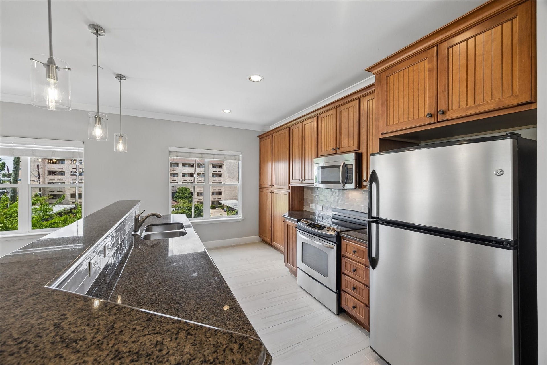 2203 Dorrington Street Street, #205, Houston, TX 77030 This modern kitchen features stainless steel appliances, granite countertops, built in beverage fridge and warm wooden cabinetry. It has ample natural light from large windows, complemented by updated stylish pendant lighting. Perfect for both cooking and entertaining, guests will be able to enjoy the open floor plan.