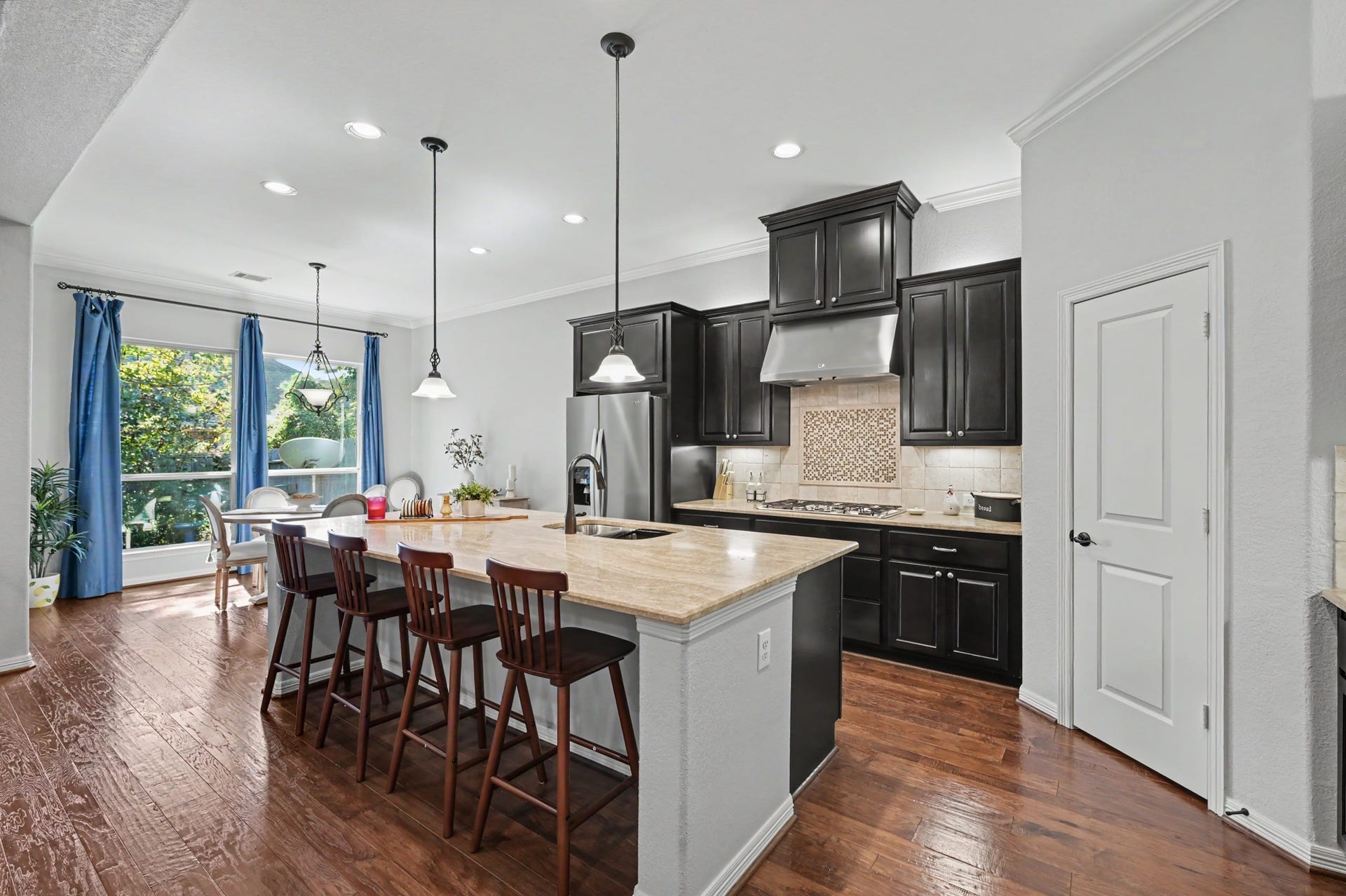 271 Rio Ranch Circle, Montgomery, TX 77316 Elegant kitchen with dark cabinetry, stainless steel appliances, and a spacious island with bar seating. The open dining area is illuminated by natural light from large windows, creating a warm and inviting atmosphere.