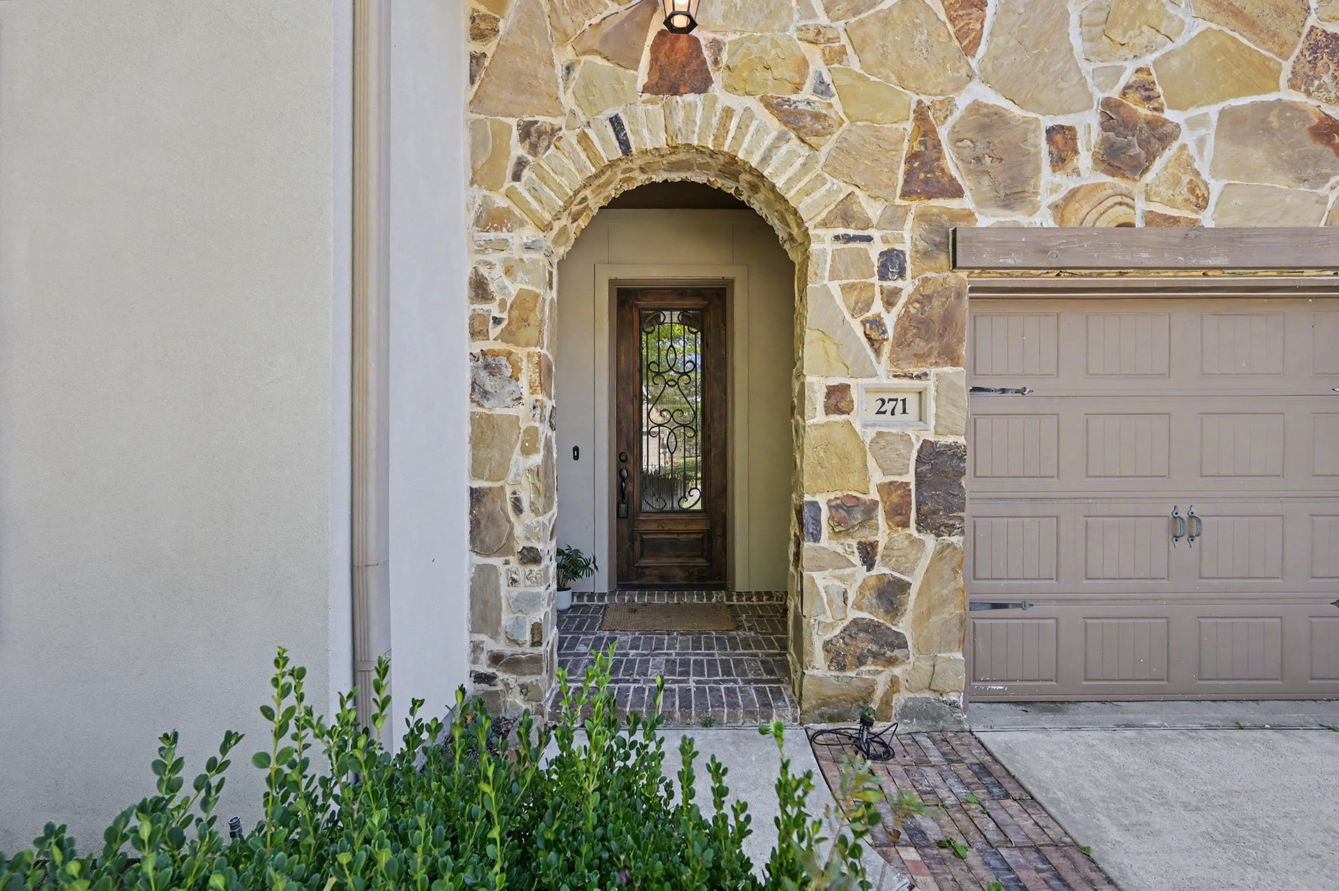 271 Rio Ranch Circle, Montgomery, TX 77316 Charming stone faade with an inviting arched entryway leads to a beautifully detailed wooden front door, complemented by a stylish garage.