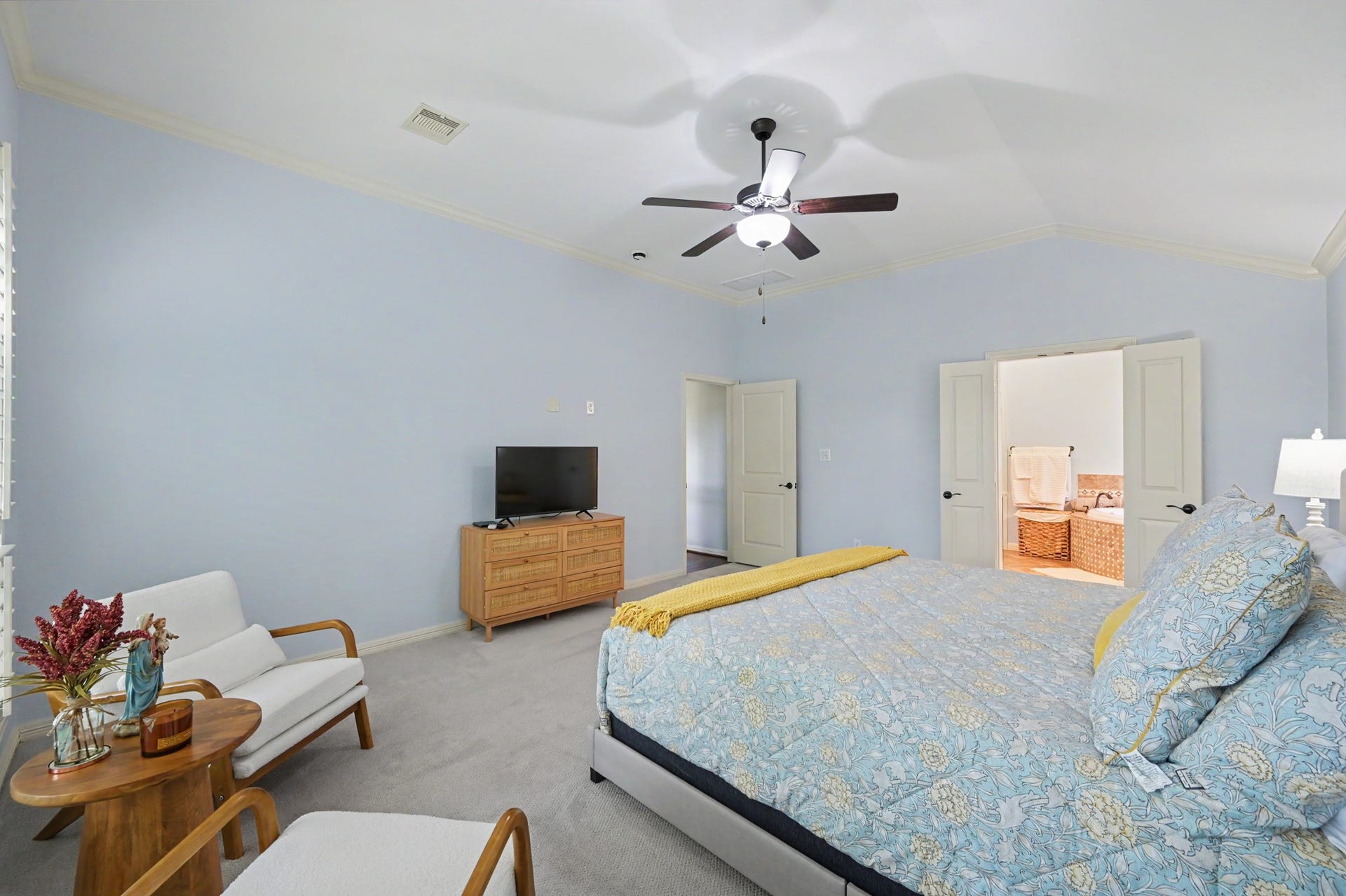 271 Rio Ranch Circle, Montgomery, TX 77316 Spacious bedroom with soft blue walls, featuring a cozy sitting area, elegant ceiling fan, and convenient ensuite bathroom access through double doors.