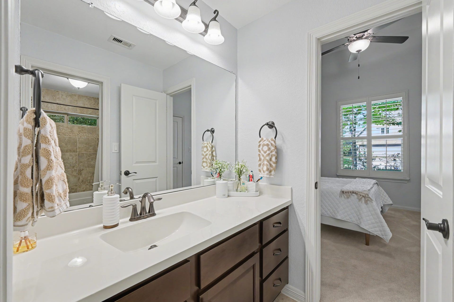 271 Rio Ranch Circle, Montgomery, TX 77316 Elegant bathroom featuring a sleek double vanity with dark cabinetry, leading into a cozy bedroom with natural light streaming through plantation shutters.