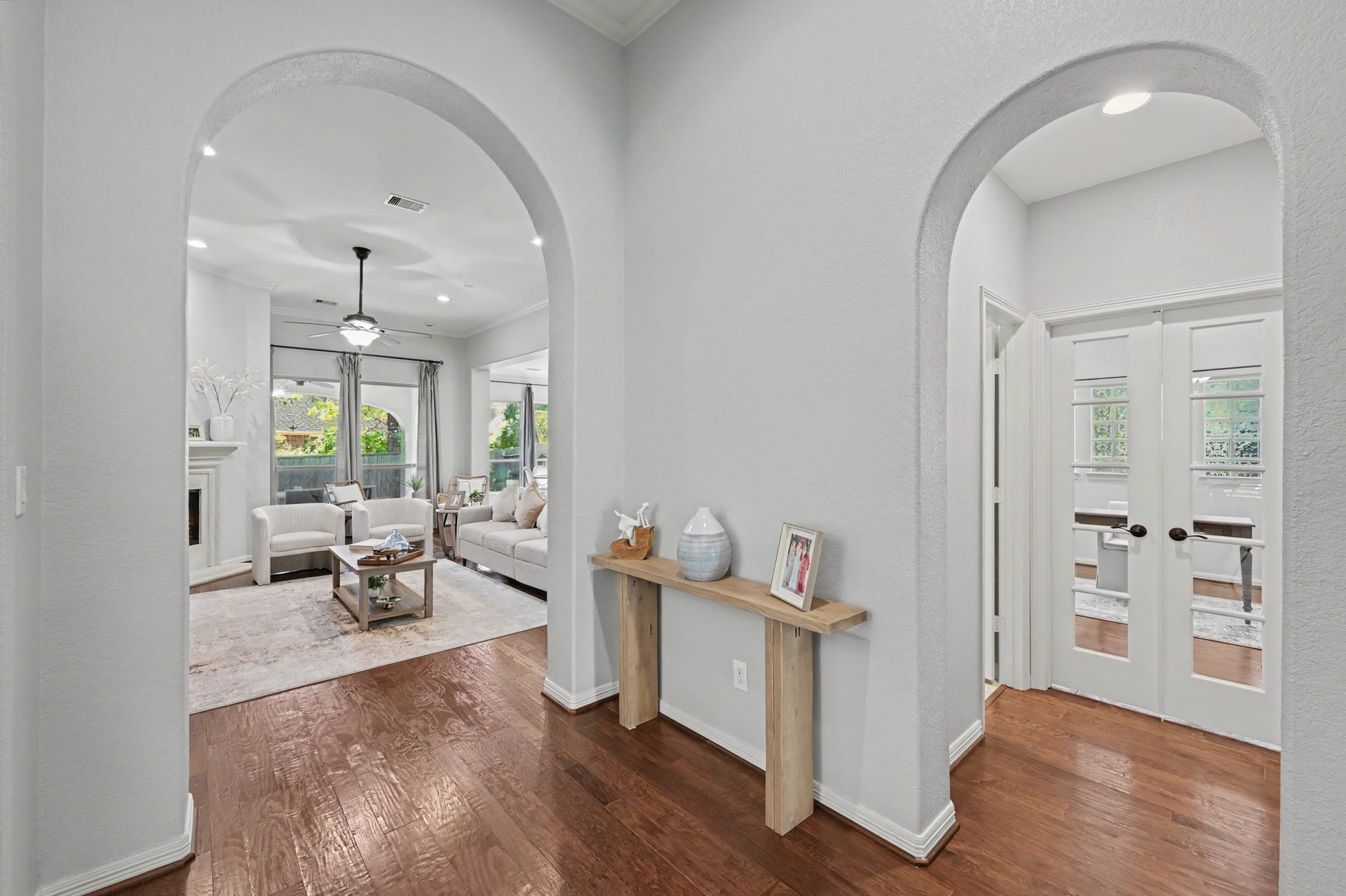 271 Rio Ranch Circle, Montgomery, TX 77316 Elegant entryway featuring arched doorways leading to a bright living room with hardwood floors and a cozy fireplace, complemented by French doors opening to a versatile office space.