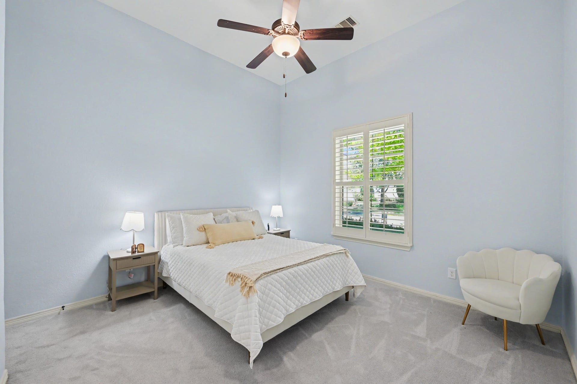 271 Rio Ranch Circle, Montgomery, TX 77316 Bright and inviting bedroom with soft blue walls, plush carpeting, and a ceiling fan for comfort. The room features a cozy bed, elegant nightstands, and a charming window with plantation shutters that allow natural light to fill the space.